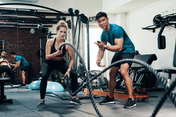 Cropped shot of an attractive young sportswoman working out with battle ropes with her personal trainer in a gym